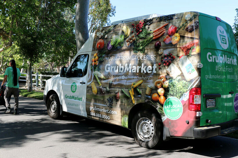 Exterior photo of a food delivery van with driver pushing a handtruck stacked with food boxes away from camera.