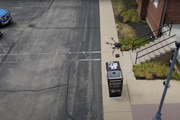 Photo of aerial drone delivering a small package into a custom built mailbox by lowering the item in with a cable.